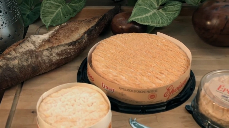 Fromage Époisses de Bourgogne à croûte orangée posé à côté d’une baguette sur une table en bois