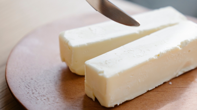 Deux bâtons de beurre doux sur une assiette en bois avec un couteau au-dessus