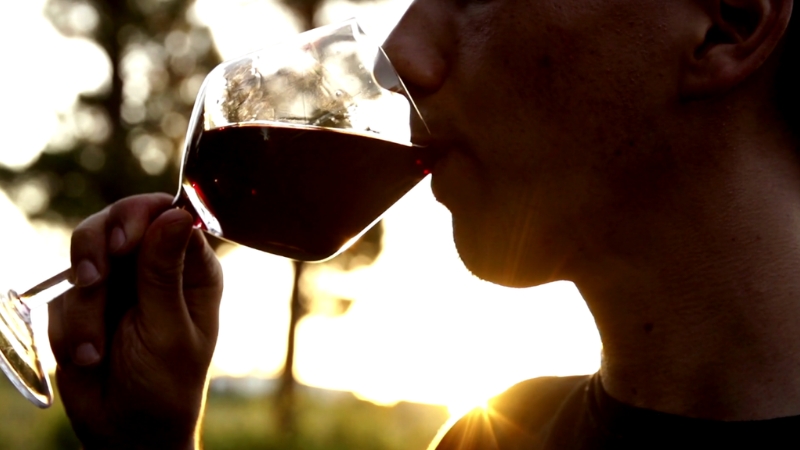 Un homme boit un verre de vin rouge au coucher du soleil