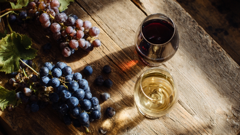Deux verres de vin rouge et blanc posés sur une table en bois avec des grappes de raisin